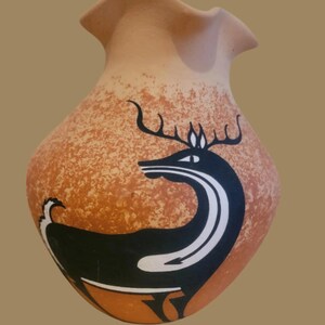 May include: A terracotta-colored vase with a speckled pattern and a ruffled rim. The vase features a black and white deer design on the front. The deer has large antlers and a curved neck. The vase is a decorative item.