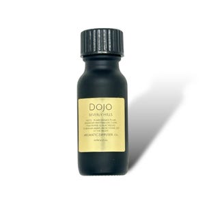 May include: A black aromatic diffuser oil bottle with a black cap and a gold label. The label reads "DOJO Beverly Hills" and lists the notes. The bottle is approximately 15 ml.