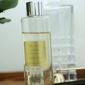 May include: A clear glass bottle with a silver lid filled with a light yellow liquid. The bottle has a yellow label with the text "Dojo Candles LA NIGHTS NOTES LEMON GINGER, AMBER LUXURY REED DIFFUSER REFILL VOLUME APPROX 6.8 FL OZ 200 ML".