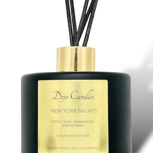 May include: Black glass reed diffuser bottle with gold lid and black reeds. The label reads "Dojo Candles New York Nights Notes: Cedar, Sandalwood, Jasmine, Amber Luxury Reed Diffuser Volume Approx. 6.8 Fl Oz (200 ml)"