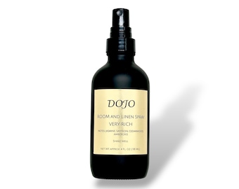 May include: A black room and linen spray bottle with a white label. The label reads "DOJO ROOM AND LINEN SPRAY VERY RICH" with scent notes listed below. The bottle contains approximately 4 fl oz (118 ml) of product.