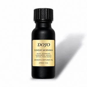 Könnte beinhalten: Eine mattschwarze Glasflasche mit schwarzem geripptem Verschluss, die aromatisches Diffusoröl enthält. Das goldene Etikett trägt den Text DOJO, SUNDAY MORNING, Noten von Agarholz, Sandelholz, Vanille, Vetiver, Tonkabohnen und ca. 15 ml.