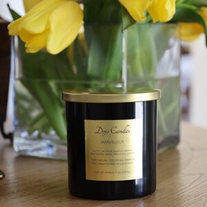 Pu&ograve; includere: Un barattolo di candela nero con un coperchio e un'etichetta dorati. L'etichetta riporta "Dojo Candles" e "Marvelous". La candela &egrave; circondata da tulipani gialli in un vaso di vetro. La candela pesa 255 grammi ed &egrave; realizzata con cera di soia 100% naturale.