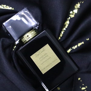 Puede incluir: Una botella de vidrio negro de la fragancia de lujo Josephine Josephine de Dyptique Candles. La botella tiene una tapa dorada y una etiqueta dorada con el nombre del producto y la marca.