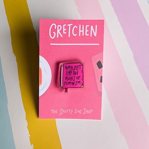 May include: Pink enamel pin with the text "That's just like the rules of feminism" on a white background. The pin is on a pink card with the text "Gretchen" and "The Spotty Dog Shop".