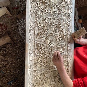 May include: A person carving intricate floral patterns into a wooden panel. The panel is covered in detailed carvings, creating a beautiful and ornate design.