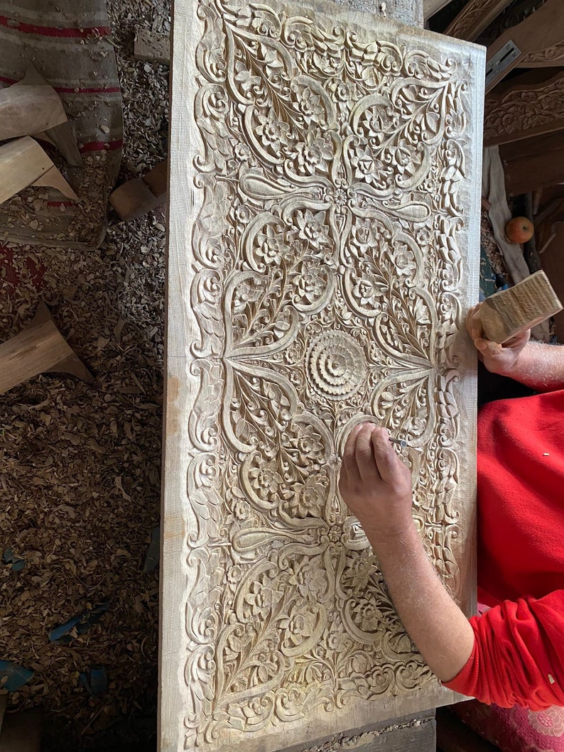 May include: A person carving intricate floral patterns into a wooden panel. The panel is covered in detailed carvings, creating a beautiful and ornate design.