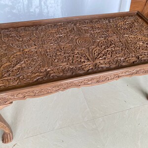 May include: A intricately carved wooden coffee table with a floral design. The table has four legs and a rectangular top.