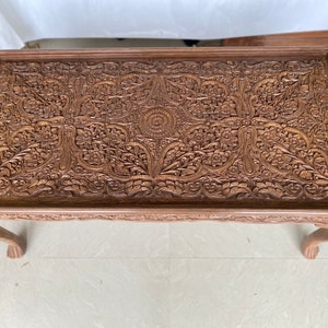 May include: A dark brown wooden coffee table with intricate carved floral designs on the top. The table has four legs.