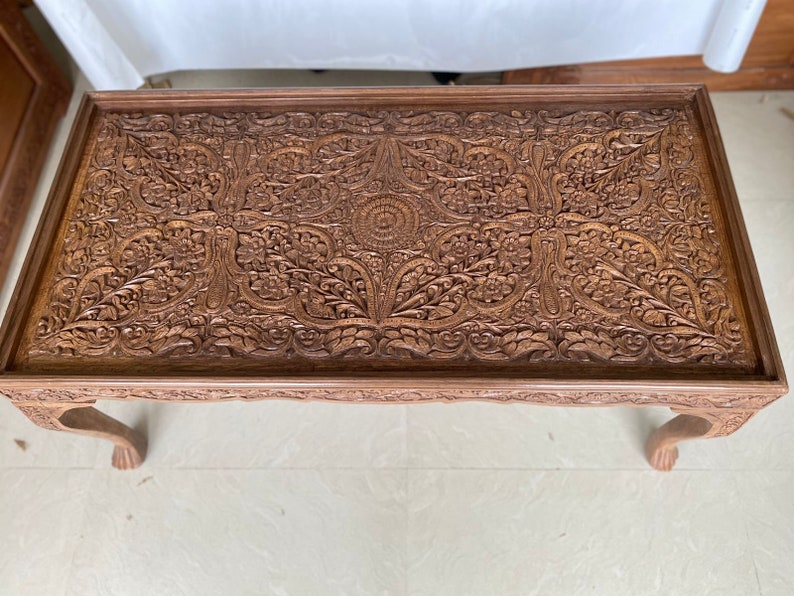 May include: A dark brown wooden coffee table with intricate carved floral designs on the top. The table has four legs.