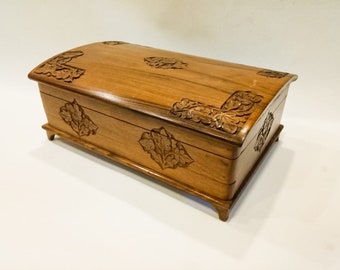 May include: A wooden box with a carved lid and floral designs. The box is made of light brown wood and has a slightly curved lid. The floral designs are carved into the wood and are very detailed.