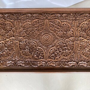 May include: A rectangular wooden tray with intricate carved floral designs. The tray is made of dark brown wood and has a raised edge.