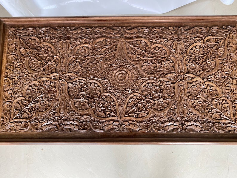 May include: A rectangular wooden tray with intricate carved floral designs. The tray is made of dark brown wood and has a raised edge.