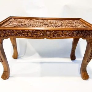 May include: A hand-carved wooden coffee table with intricate floral designs on the top and legs. The table has a rich brown color and a rectangular shape.