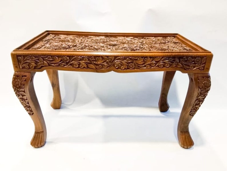 May include: A hand-carved wooden coffee table with intricate floral designs on the top and legs. The table has a rich brown color and a rectangular shape.