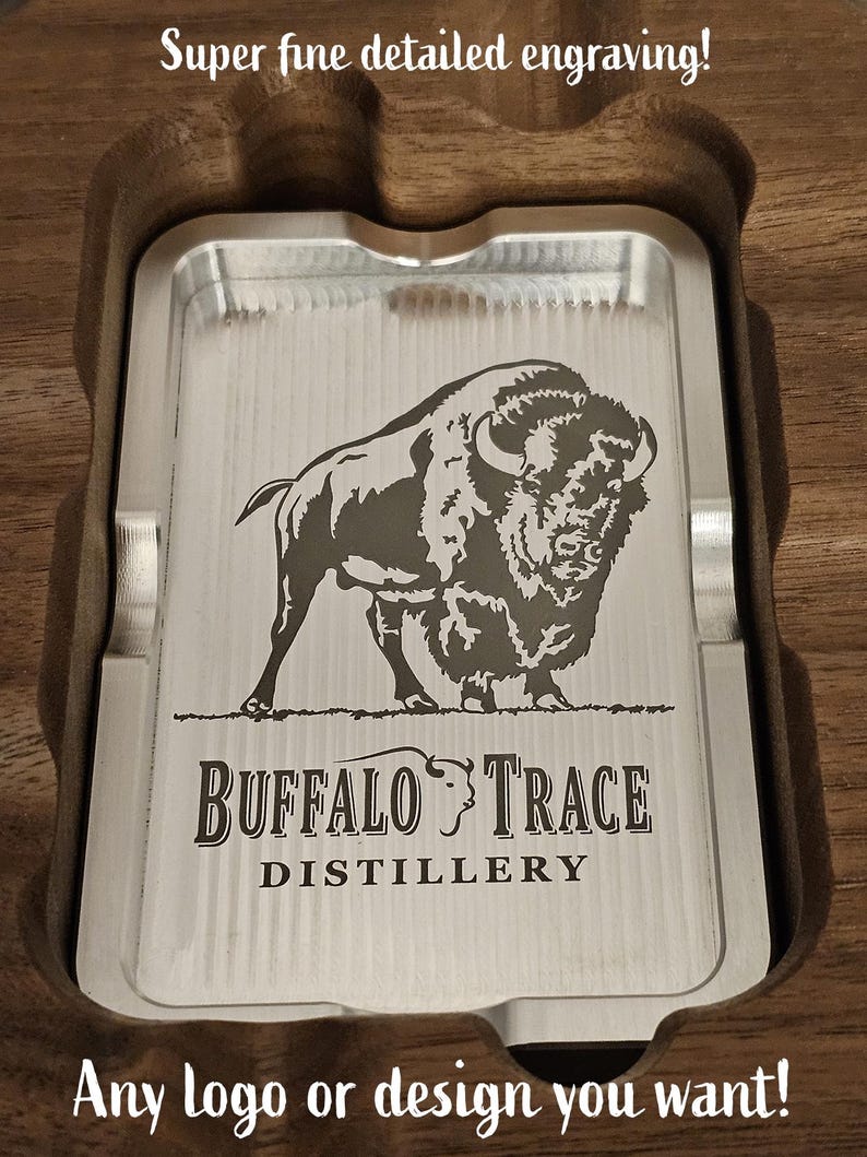 Puede incluir: Una bandeja rectangular plateada con el logotipo de Buffalo Trace Distillery y un grabado de bisonte, colocada en un soporte de madera. El texto en la parte superior dice "Super fine detailed engraving!" y en la inferior "Any logo or design you want!"