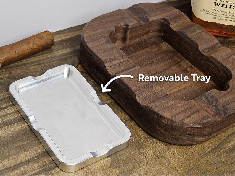 Puede incluir: Un cenicero de cigarros de madera con una bandeja plateada extra&iacute;ble. El cenicero es de madera oscura y tiene un dise&ntilde;o curvo. Un cigarro descansa sobre la superficie de madera. El texto "Removable Tray" es visible.