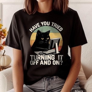 May include: Black t-shirt with a graphic of a black cat at a computer, with the text "HAVE YOU TRIED TURNING IT OFF AND ON?" in white. The cat is in front of a retro sunset background.