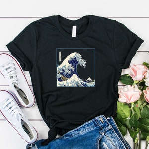 Op de afbeelding: Zwart T-shirt met een grafische print van de Grote Golf voor Kanagawa, een beroemde Japanse houtsnede van Hokusai. De print toont een grote golf met de berg Fuji op de achtergrond.