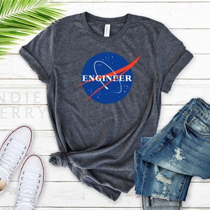 Op de afbeelding: Een donker grijs t-shirt met een blauw en rood NASA-geïnspireerd logo met de tekst "Engineer".