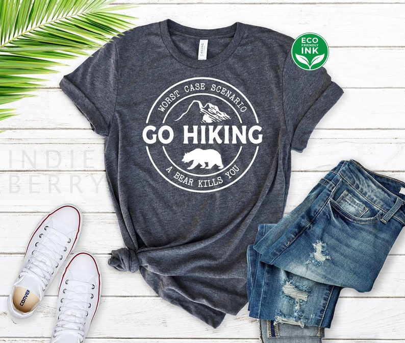 May include: A dark gray t-shirt with a white circle graphic that says "Worst Case Scenario Go Hiking A Bear Kills You". The graphic also includes a mountain range and a bear.