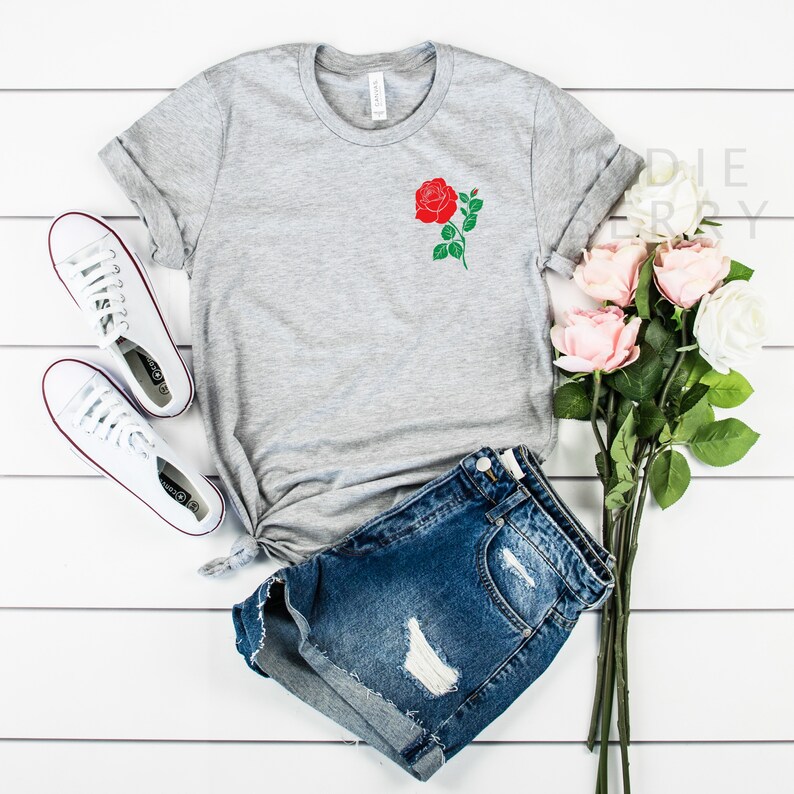 May include: A gray t-shirt with a red rose graphic on the left chest. The shirt is paired with denim shorts and white sneakers.