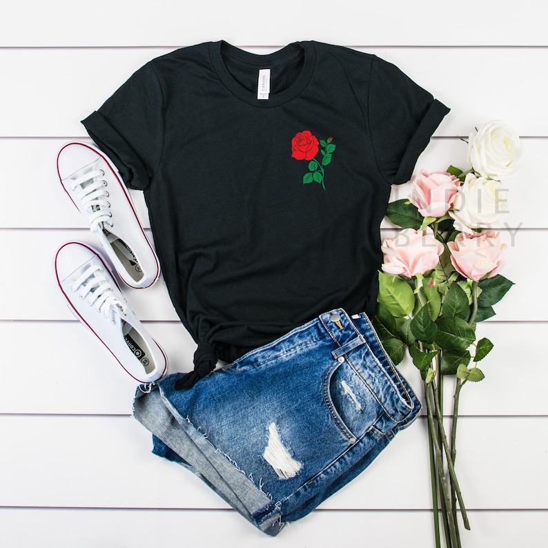 May include: Black t-shirt with a red rose graphic on the front. The shirt is paired with denim shorts and white sneakers.