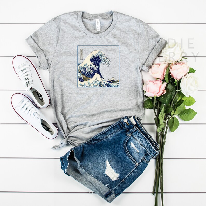 Op de afbeelding: Grijs T-shirt met een grafische print van de Grote Golf voor Kanagawa, een beroemde Japanse houtsnede van Hokusai. De print toont een grote golf met de berg Fuji op de achtergrond.