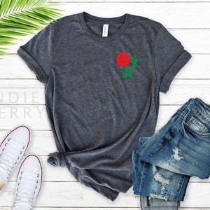 May include: A dark gray t-shirt with a red rose embroidered on the left chest. The rose has green leaves and a stem.