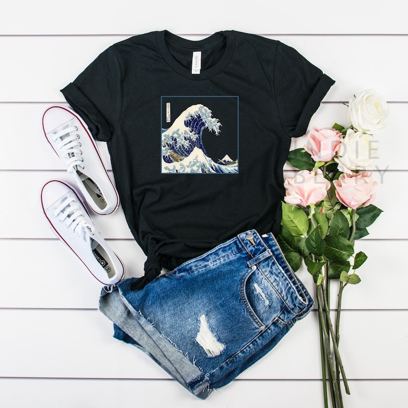 Op de afbeelding: Zwart T-shirt met een grafische print van de Grote Golf voor Kanagawa, een beroemde Japanse houtsnede van Hokusai. De print toont een grote golf met de berg Fuji op de achtergrond.