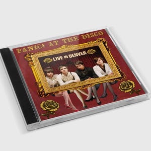 May include: A CD case featuring the text "Panic! At The Disco" at the top. The cover has a maroon background with a gold ornate frame around a photo of the band. The text "Live in Denver" is inside the frame.