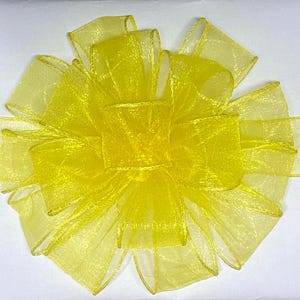 May include: A bright yellow decorative bow made of sheer ribbon. The bow is layered and has multiple loops and tails, creating a full and textured appearance. The edges of the ribbon are finished with a subtle gold trim.