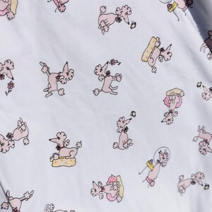 Pode incluir: Tecido branco com um padrão repetido de poodles cor-de-rosa em várias poses. Os poodles usam laços e alguns estão segurando objetos como um bolo ou uma bola.