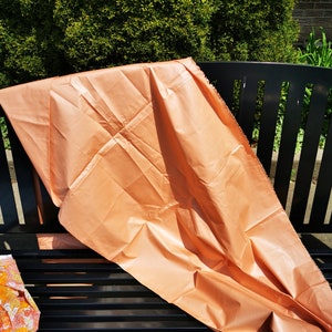 Puede incluir: Un gran trozo de tela de color melocotón está drapeado sobre un banco de metal negro. La tela es lisa y brillante, y parece estar hecha de un material ligero.