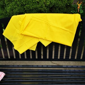 Könnte beinhalten: Ein leuchtend gelber Stoff, der über eine schwarze Metallbank gelegt ist. Der Stoff ist in der Mitte gefaltet und hat eine glatte Textur.