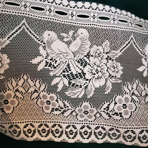 May include: White lace fabric with a floral and bird pattern. The lace features a detailed design with flowers, leaves, and birds, creating an intricate and delicate texture. The fabric is likely used for decorative purposes.