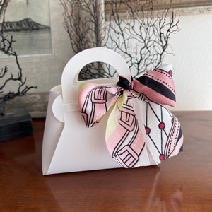 May include: A white paper handbag with a pink and black patterned ribbon tied around the handle.