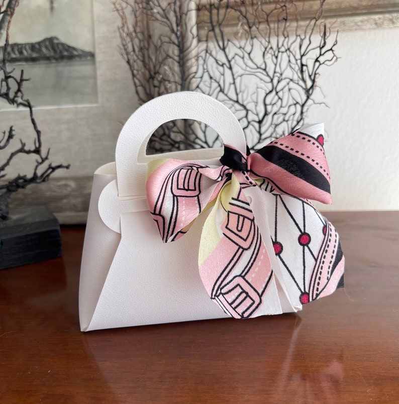 May include: A white paper handbag with a pink and black patterned ribbon tied around the handle.
