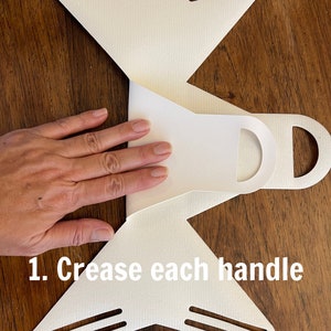 May include: White paper mask with two handles on each side. The text "1. Crease each handle" is printed on the bottom of the mask.