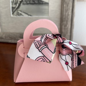 May include: A small pink handbag with a white and pink patterned ribbon tied around the handle.