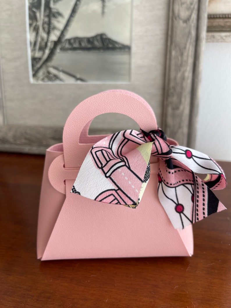 May include: A small pink handbag with a white and pink patterned ribbon tied around the handle.