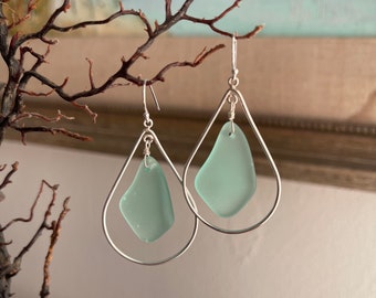 May include: A pair of silver hoop earrings with a light blue sea glass charm hanging from each hoop.