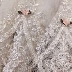 Puede incluir: Tela de encaje blanca con delicado bordado floral y rosas de sat&eacute;n rosa.