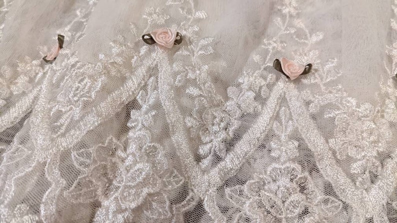 Puede incluir: Tela de encaje blanca con delicado bordado floral y rosas de sat&eacute;n rosa.