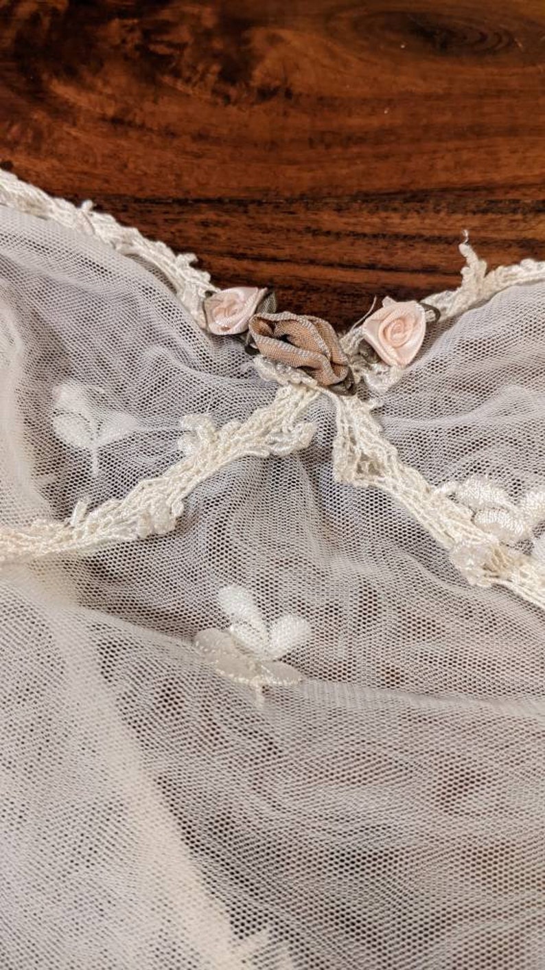 Puede incluir: Tela de encaje blanca con un delicado patr&oacute;n floral y una cinta rosa atada en un lazo.