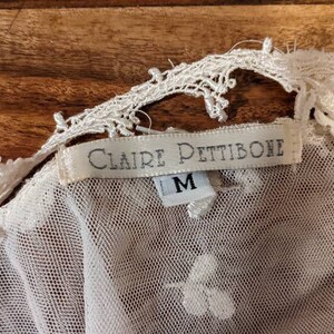 Puede incluir: Top de encaje blanco con una etiqueta blanca que dice "Claire Pettibone" y "M" para el tama&ntilde;o.