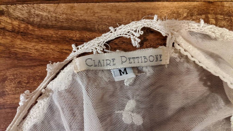 Puede incluir: Top de encaje blanco con una etiqueta blanca que dice "Claire Pettibone" y "M" para el tama&ntilde;o.