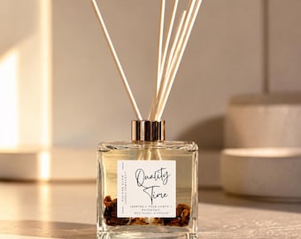 May include: A square glass reed diffuser bottle with a gold cap and six wooden reeds. The white label reads Quality Time, Jasmine, Palo Santo, Patchouli, and 8oz (226g) Diffuser. Dried botanicals are visible at the bottom of the clear liquid.
