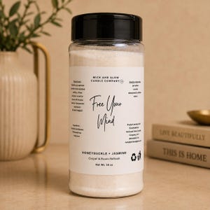 May include: A clear plastic bottle with a black screw-top lid containing white carpet and room refresh powder. The label reads Wick and Glow Candle Company, Free Your Mind, Honeysuckle + Jasmine, and Net Wt. 16 oz, with usage instructions and ingredients.