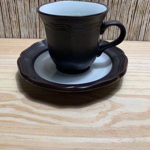 May include: A brown and white ceramic coffee cup and saucer set. The cup has a rounded shape and a white interior. The saucer has a scalloped edge.